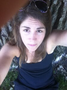 Jess in black tank top leaning against the trunk of an oak tree, ashes shown spread near the base of the tree.